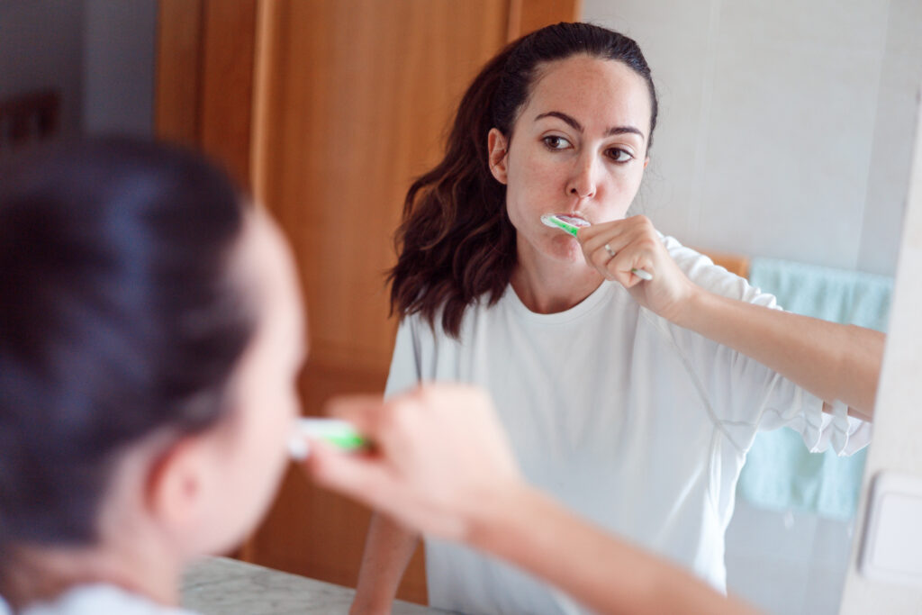 Smiling young woman brushing teeth in bathroom