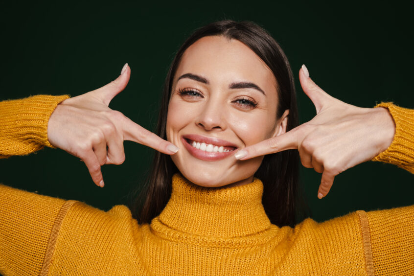 joyful beautiful girl smiling and pointing fingers at her with white perfect set of teeth