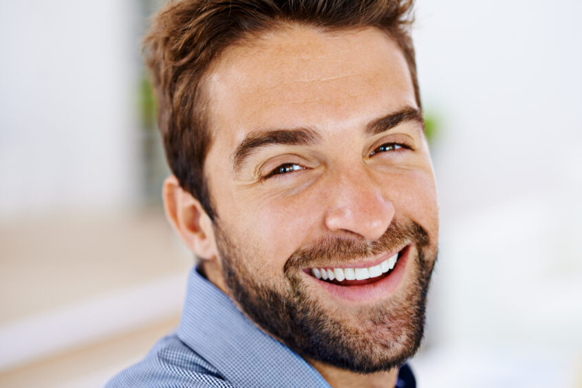 man in blue shirt with white teeth smiling in side view